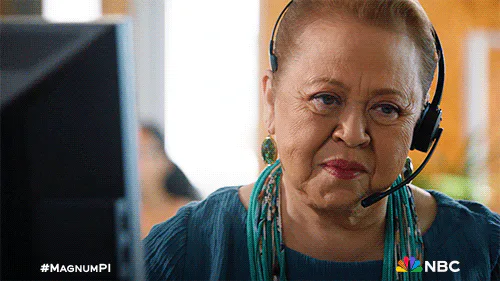 An older woman with a headset and a teal necklace looks up with a serious expression.