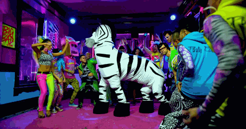 Dancers in neon 1980s outfits move around a life-size zebra costume in a purple-lit club scene.