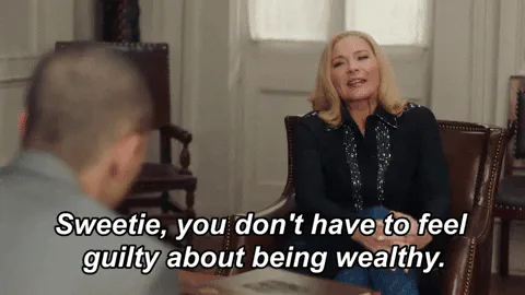 A blond woman in a black blouse sits across a desk and says, 'Sweetie, you don't have to feel guilty about being wealthy.'