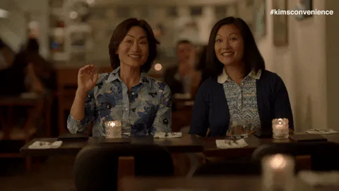 Two women wave and smile together at a candlelit restaurant table.