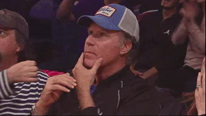 A man in a trucker cap sits courtside stroking his chin with a skeptical, appraising look.