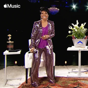 Patti+Labelle+Dancing+GIF+by+Apple+Music.gif A woman in a sparkly purple suit sings into a microphone on a flower lined stage.