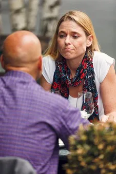 A woman speaks with a bald man across a restaurant table.