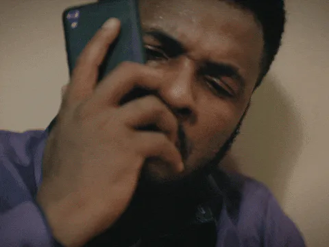 A man in a purple shirt squints and grimaces while staring closely at his phone screen.