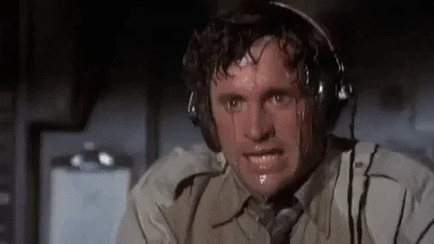 A sweaty man wearing a headset wipes his forehead, looking distressed and tense.