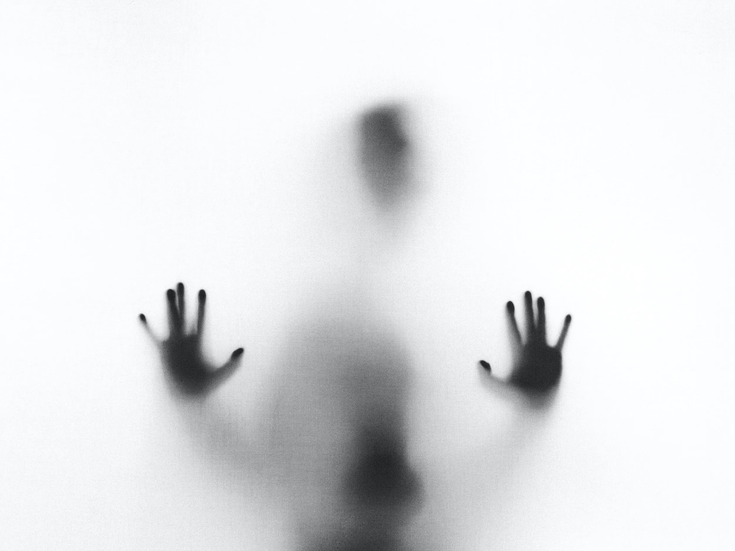 A blurred human silhouette presses both hands against frosted glass in black and white.