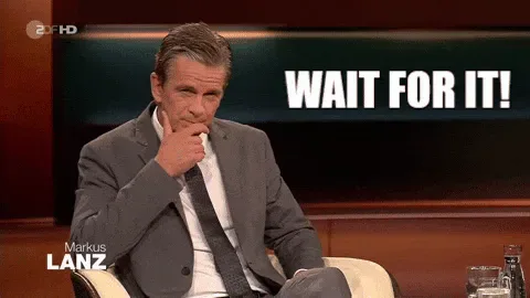 Wait+For+It+GIF+by+ZDF.gif A man in a suit sits thoughtfully with a hand on his chin and says 'Wait for it!'