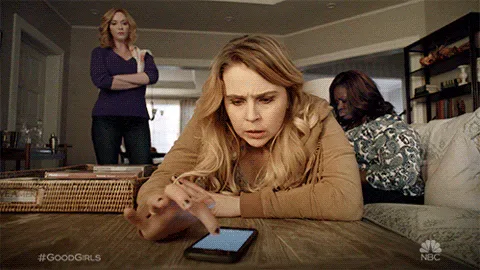 Frustrated+Good+Girls+GIF+by+NBC.gif A woman leans over a phone on a table looking troubled, while two women watch from a couch behind her.