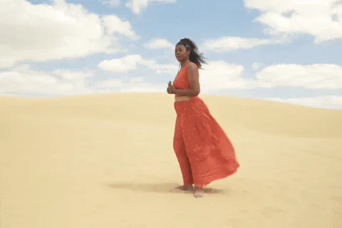 Animated reaction GIF of a woman in a flowing red dress walking across a sunny beach.
