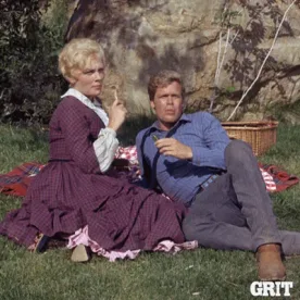 Date+Night+Love+GIF+by+GritTV.gif A blonde woman in a vintage dress laughs while sitting on a picnic blanket with a man beside her.