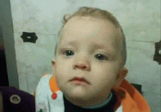 A baby with a pouty, tearful expression looks down and turns away.