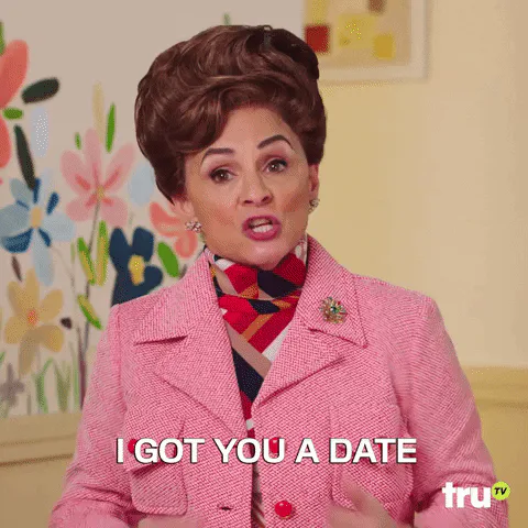 A woman with a bouffant hairstyle in a pink coat gestures and says 'I got you a date.'