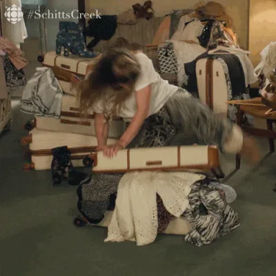 Schitts+Creek+Comedy+GIF+by+CBC+(3).gif A woman with long hair playfully tumbles face-first into an open suitcase piled with clothes.
