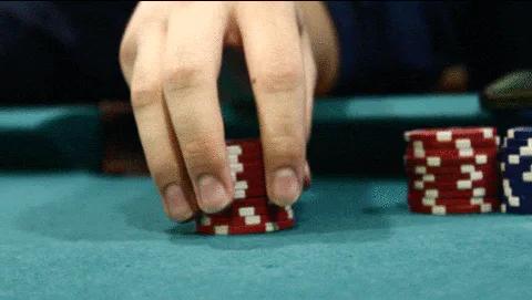 A close-up of hands stacking and restacking red poker chips on a green felt table.