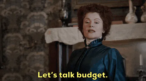 A woman in a Victorian-style dress speaks as on-screen text reads 'Let's talk budget.'