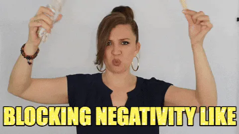 A woman holds a can and a pencil overhead, spraying around her, captioned 'Blocking negativity like.'