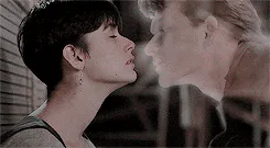A man and woman in profile lean close together with smoke drifting between their faces.