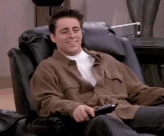 Sad+Season+2+GIF+by+Friends.gif A man in a brown jacket laughs while relaxing in a leather recliner, holding a remote control.