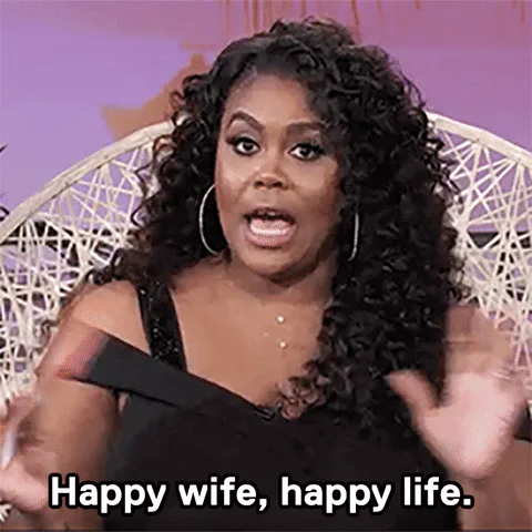 A woman with curly hair gestures while saying 'Happy wife, happy life.'