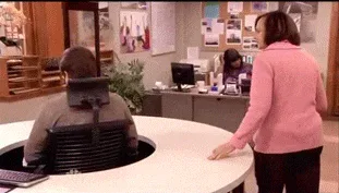 Parks+And+Rec+Spinning+GIF.gif In an office with a round desk, a man sits at a lowered computer station as a coworker in pink looks on.