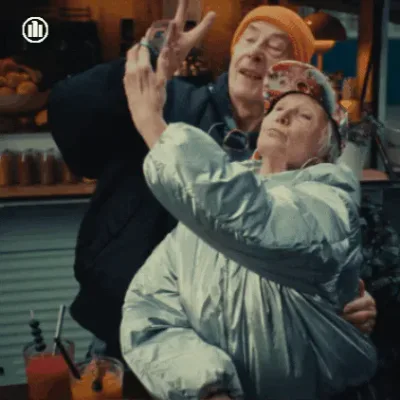Social+Media+Love+GIF+by+AllianzDeutschland.gif An older couple pose for a selfie together at an outdoor bar counter, smiling.