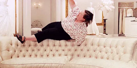 melissa+mccarthy+television+GIF+by+Saturday+Night+Live.gif A woman in a floral top tumbles backward onto a cream sofa in a bridal shop.